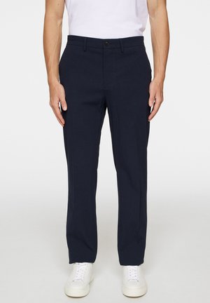 Navyblauwe op maat gemaakte broek van lichtgewicht stof, met een slim fit, zijzakken en een voorplooidetail, gecombineerd met witte sneakers.