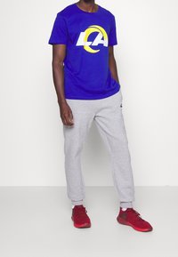 Modrý tričko s bílým a žlutým logem "LA"; šedé tepláky; červené sportovní boty. Jednoduchý, ležérní sportovní design.