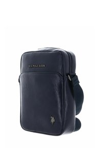 Sac bandoulière en cuir bleu marine avec logo U.S. Polo Assn., fermeture zippée, sangle réglable et deux poches latérales pour un rangement supplémentaire.