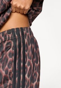 Spodnie dresowe w panterkę w połączeniu różowego i czarnego materiału; posiadają czarne paski po bokach i elastyczną talię z subtelnym połyskiem.