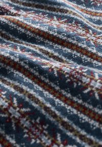 Strickwollstoff mit blauer Hintergrundfarbe, versehen mit weißen, roten und grünen Blumenmustern, die in horizontalen Streifen angeordnet sind. Strukturierte Oberfläche.
