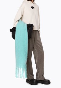 Felpa crema con dettagli ricamati neri, giacca a vento scura, sciarpa fluffy verde menta, pantaloni a scacchi testurizzati e scarpe nere con piattaforma.