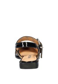 Zwarte lakleren sandalen met verstelbare enkelband, open achterkant en lage hak. Lichtbruine voetbed heeft ronde perforaties.