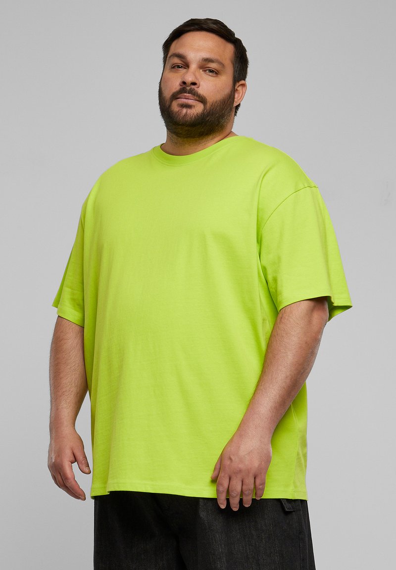 T-shirt in cotone verde neon con una vestibilità rilassata, maniche corte e scollo a girocollo, abbinato a pantaloni scuri. Texture liscia.