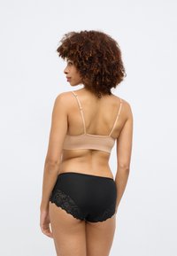 Nøgen bralette med justerbare stropper, parret med sorte trusser med blonder detaljer. Glat stofstruktur med en sømløs design.