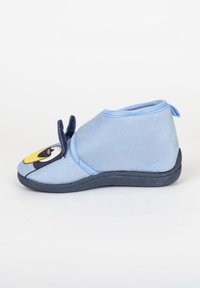 Zapatilla de tela azul con punta redondeada, que presenta un diseño de cara de dibujo animado en amarillo y negro, y una parte superior suave y texturizada. Suela de goma plana.