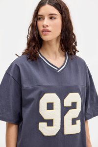 Πλοίαρχος μπλε υπερμεγέθη μπλούζα με v-neck, λευκή και γκρι ριγωτή γιακά και υφή κρεμ χρώματος "92" στη μπροστινή πλευρά. Μαλακό ύφασμα.