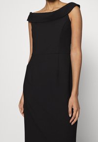 Schwarzes Kleid mit schulterfreiem Halsauschnitt, enganliegendem Oberteil und einer glatten, eleganten Textur. Verfügt über eine Seitentasche und keine sichtbaren Muster.