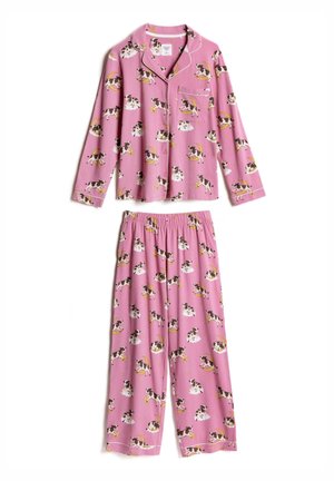 Femme aux longs cheveux bruns portant un pyjama rose à boutons avec des imprimés de vaches noires et blanches sur des lunes et des nuages.