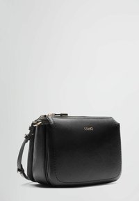 Sac en cuir noir à bandoulière avec une finition texturée, accents en métal doré, fermeture éclair, et logo en relief à l'avant.