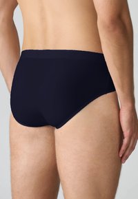 Slip da bagno blu navy realizzati in tessuto liscio, caratterizzati da un taglio a vita bassa e cuciture minime, con una morbida cintura elastica.
