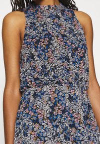 Vestido sin mangas con un estampado floral de flores azules, rosas y blancas sobre un fondo oscuro. Tejido ligero con cintura fruncida.