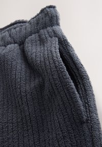 Dark gray ribbed fabric with a soft, textured surface, features a gathered waistband and a side opening, creating a relaxed look.