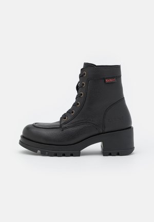 Bottine noire en cuir à lacets, talon épais et semelle crantée, avec une petite étiquette de marque Kickers rouge et noire sur le côté.