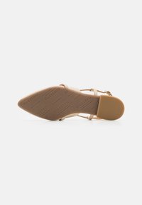 Beige ankle strap high-heeled sandal with pointed toe, textured rubber sole, and embossed brand logo on the bottom.