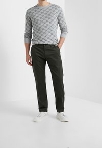 Maglione grigio con motivo, con colletto tondo, abbinato a pantaloni verdi scuri e sneakers bianche, tutto su uno sfondo bianco semplice.