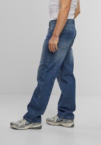 Denim jeans i middels blå, rett ben-design med falmet finish, med en baklomme og slitt tekstur, paret med joggesko.
