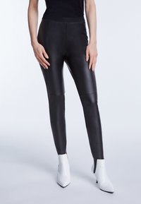 Svarta faux läderleggings med en slät yta, som har hög midja och en figurnära design, kombinerade med vita spetsiga ankelstövlar.