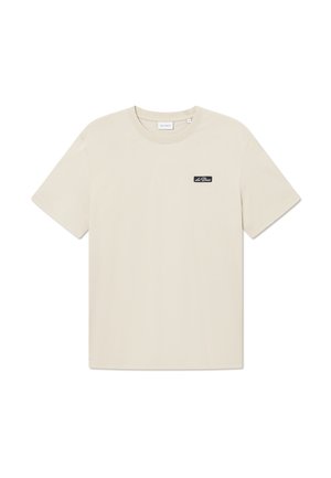 Beige Baumwoll-T-Shirt mit kurzen Ärmeln und Rundhalsausschnitt, ausgestattet mit einem kleinen schwarzen Logoaufnäher auf der linken Brust. Glatte Textur.