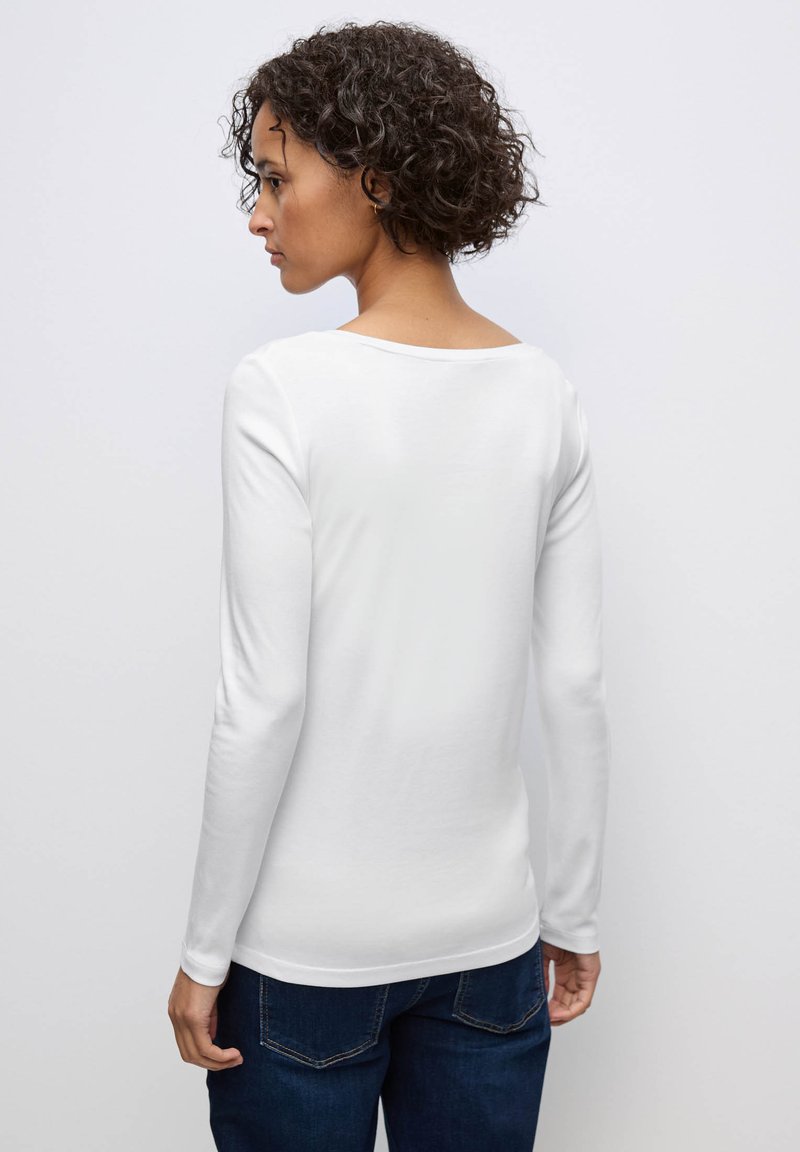 Wit longsleeve top van zachte stof, met een ruime halslijn en slim fit, gecombineerd met donkere jeans. Het achteraanzicht toont naadloze constructie.