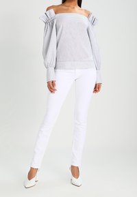 Top de rayas sin hombros con mangas abullonadas, en azul claro y blanco, combinado con pantalones ceñidos blancos y tacones blancos.