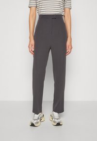 Pantalon gris sur mesure à devant plat, fermeture par bouton, coupe slim, associé à des baskets métalliques et une chemise rayée.