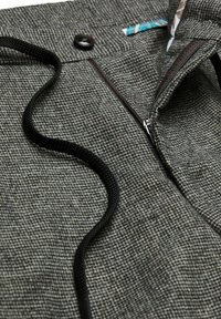 Grauer Strukturstoff mit einem Hahnentrittmuster, ausgestattet mit einem schwarzen Reißverschluss und Kordelzug, akzentuiert mit einem blauen und gemusterten Etikett.