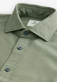 Khaki-grünes Hemd mit Knöpfen aus strukturiertem Baumwollstoff, mit Kragen, Knopfleiste und zwei dunkelblauen Knöpfen.