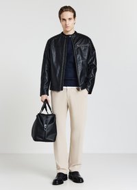 Giacca in pelle nera con chiusura a zip e spalle testurizzate, maglione di maglia blu navy, pantaloni beige e una borsa nera strutturata. Scarpe nere.