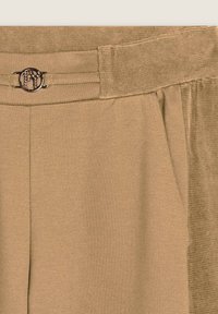 Pantaloni beige con una cintura testurizzata, caratterizzati da un accento metallico del logo. Il tessuto appare morbido con una finitura liscia.