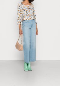 Haut court fleuri à manches bouffantes, jean taille haute bleu clair, bottines vert menthe et sac à main beige texturé.