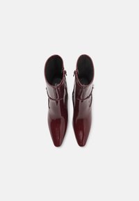 Burgundowe lakierowane botki za kostkę z ostrym noskiem, zamkiem błyskawicznym z boku i gładką teksturą. Minimalistyczny design bez widocznych wzorów.