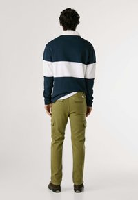 Marineblå og hvidstribet pullover, bomuldsblanding, med krave. Olivengrøn cargo-bukser med sidelommer. Model vender væk, mørke sko.