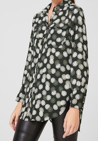 Camicia a maniche lunghe realizzata in tessuto leggero di colore verde scuro con motivo floreale, dotata di due taschini sul petto e polsini abbottonati.