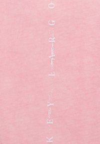 Maglietta rosa realizzata in morbido cotone. Testo verticale bianco con la scritta "KEY LARGO". Tessuto liscio con leggero effetto sbiadito sul testo.