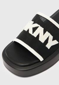 Șlapi negri cu partea superioară din plasă texturată și un logo alb proeminent, complectați de o talpă platformă neagră netedă.