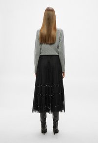 Γκρι πλεκτή μπλούζα συνδυασμένη με μαύρη δαντελένια φούστα με μαργαριταρένιες λεπτομέρειες, φορεμένη με μαύρες ψηλοτάκουνες μπότες μέχρι το γόνατο.