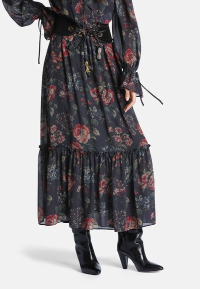Longue robe fleurie foncée avec un ourlet volanté, associée à des bottines noires à bouts pointus et à talons, ainsi qu'une large ceinture noire avec des liens en dentelle.