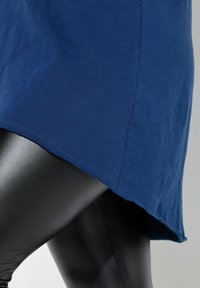 Top blu navy con orlo leggermente irregolare, realizzato in tessuto leggero. Abbinato a leggings neri lucidi, eleganti.