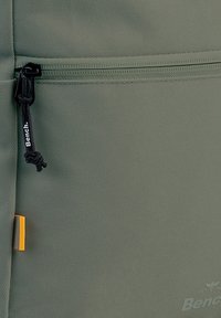 Groene stoffen rugzak met een ritszak en een zwarte trekhaak. Opvallende accenten met een kleine oranje detail. Textuur oppervlak.