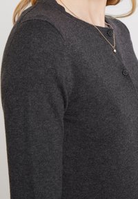 Ciemnoszary, dopasowany kardigan z okrągłym dekoltem, prążkowaną fakturą i dwoma czarnymi guzikami z przodu. Miękka, lekka tkanina.