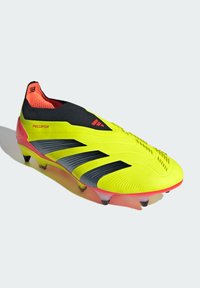 Crampon de football jaune vif avec des rayures noires et des accents rouges. Présente une tige texturée et un design élégant et aérodynamique.