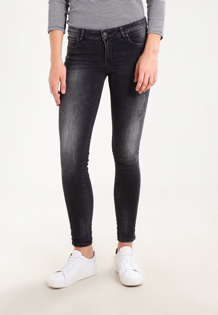 Personne portant un jean skinny noir décoloré avec une légère détresse sur une cuisse, des baskets blanches et un haut à rayures noires et blanches à manches longues.