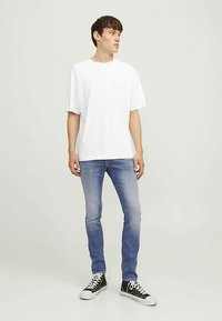 Bijela pamučna majica kratkih rukava uparena s svijetloplavim teksas trapericama. Crno-bijele tenisice zaokružuju izgled.