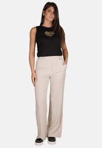 Top nero senza maniche con grafica a forma di cuore, abbinato a pantaloni larghi beige chiaro. Modello con sneakers nere. Design semplice e moderno.