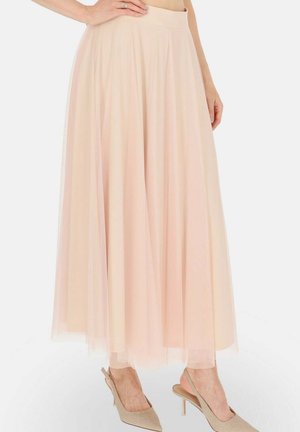 Jasnoróżowa, zwiewna spódnica midi z tiulu, noszona z cielistymi szpilkami typu slingback, dłoń modelki spoczywa na talii.