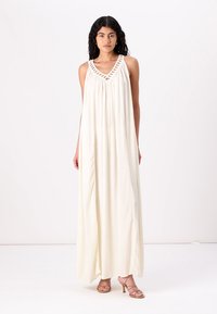 Robe longue blanche sans manches avec un décolleté en V, présentant des détails tissés le long des épaules et un tissu fluide et léger.