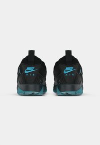 Un paio di sneakers Nike Air nere e teal viste da dietro, con il logo Nike Swoosh e il logo Jumpman visibili sui talloni.