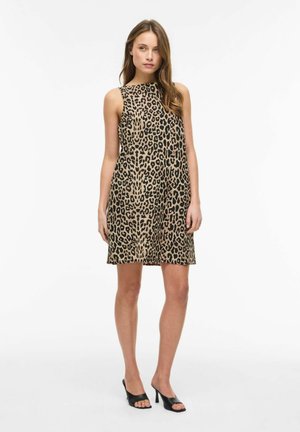 Mujer con vestido sin mangas hasta la rodilla con estampado de leopardo y mules negras de tacón alto con punta abierta, de pie sobre fondo blanco.