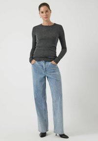 Szara bluzka z długim rękawem i okrągłym dekoltem, zestawiona z jasnoniebieskimi szerokimi spodniami dżinsowymi i czarnymi szpilkami z ostrym czubkiem. Prosty i czysty design.